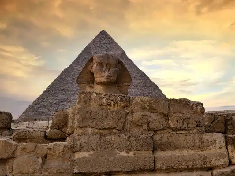 Great Sphinx in front of a Giza pyramid at sunset